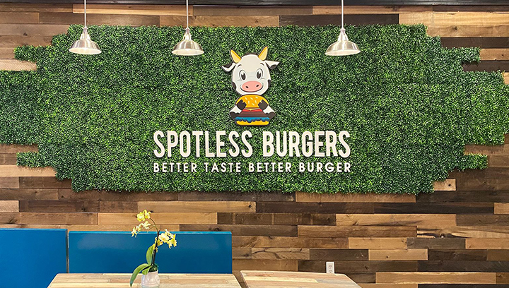 Spotless Burgers custom PVC sign with the brand name and logo on a grass wall