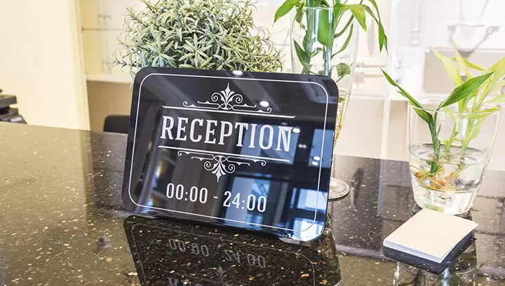 Informative lobby signs for a reception desk displaying its operating hours in black