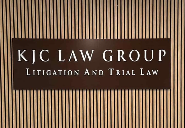 Metallic lobby signs for KJC Law Group on a wooden panel showcasing the company name