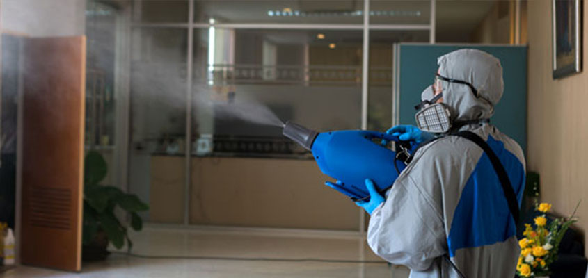 Man in protective clothing disinfecting workspace after business reopening