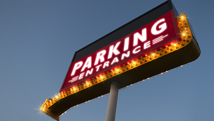 Illuminated high rise sign with a directional arrow displaying the words Parking Entrance