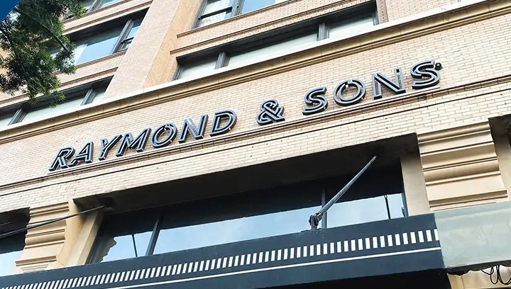 Building signs for Raymond and Sons with a stylish font in black fixed on a brick wall