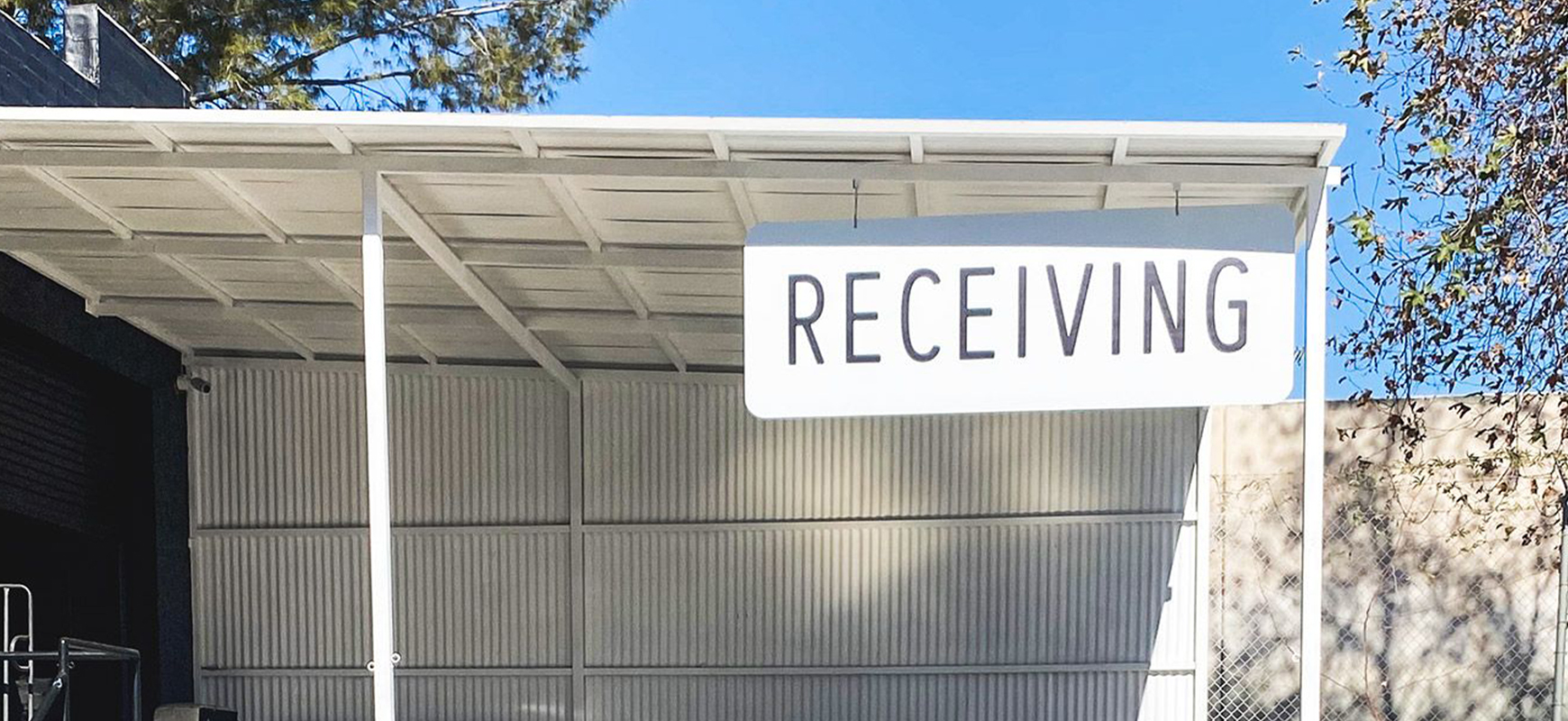 a white-colored hanging outdoor sign displaying the word Receiving