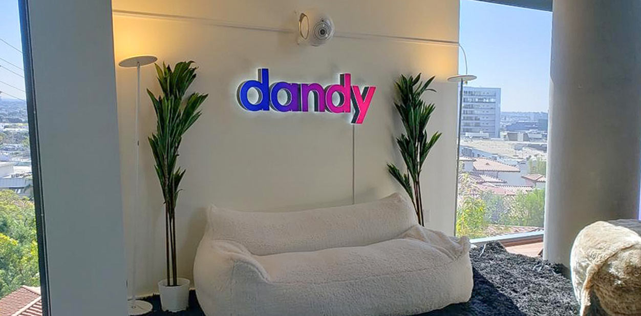 Dandy colorful letters attached on the reception wall above the white sofa and between two tall plants