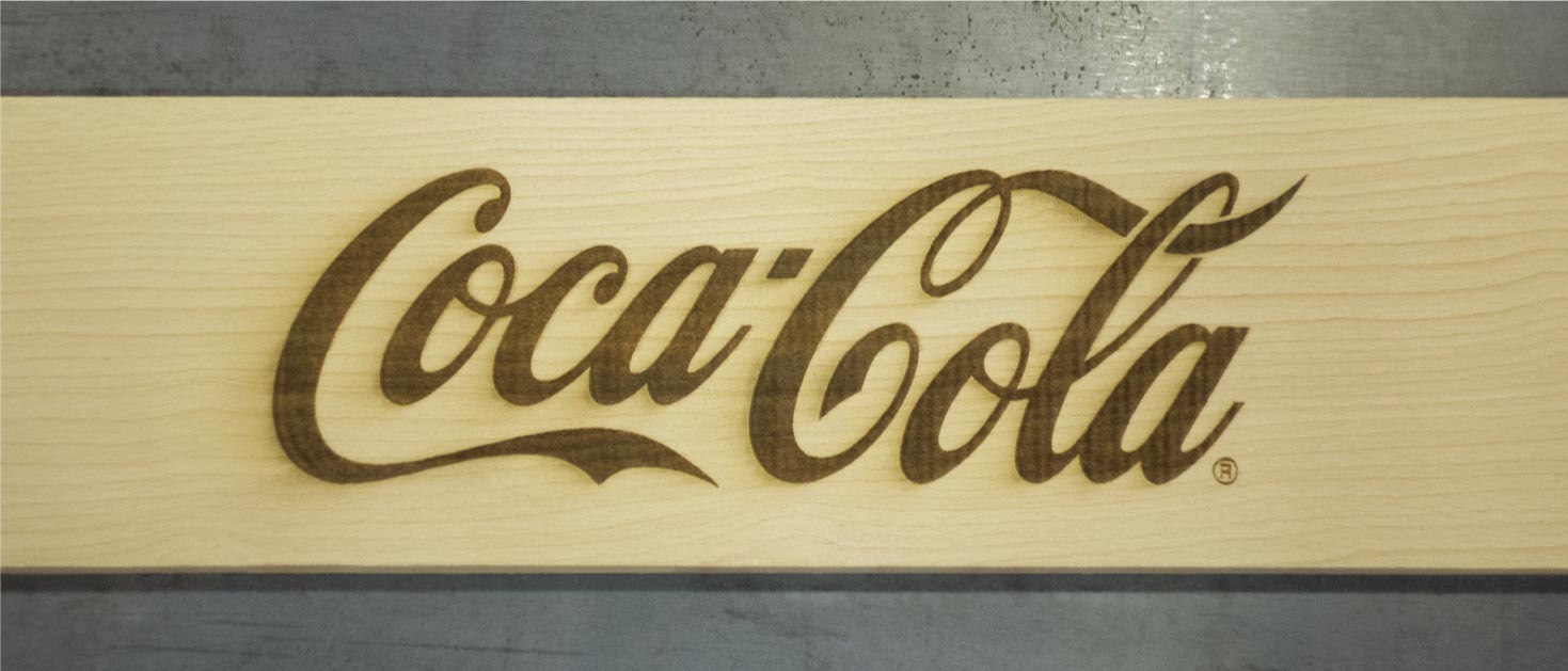 Coca-Cola logo laser engraving process on a wooden plaque for branding purposes