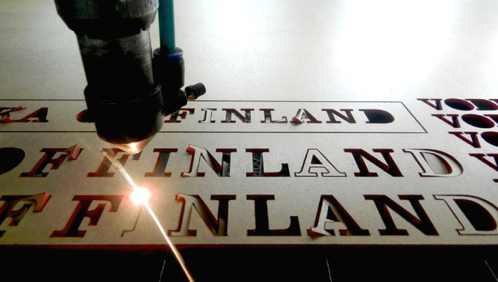 Finland laser cutting process making cut-outs of the word on a plexiglass surface