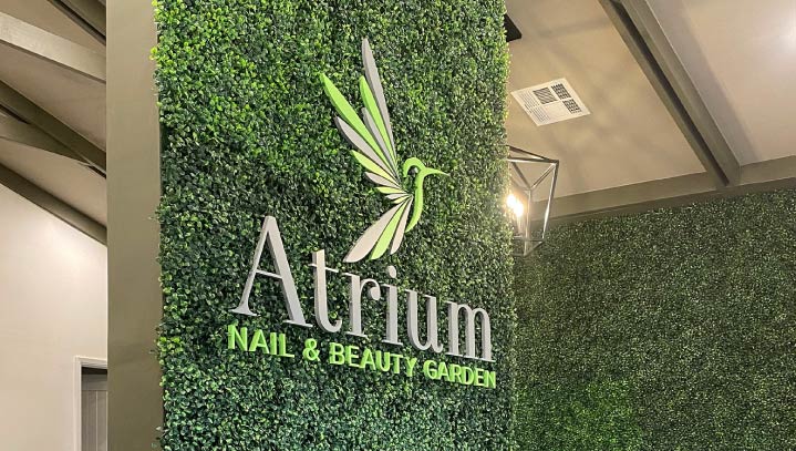 Atrium Nail & Beauty Garden custom wall sign made of acrylic and displayed on a green setting