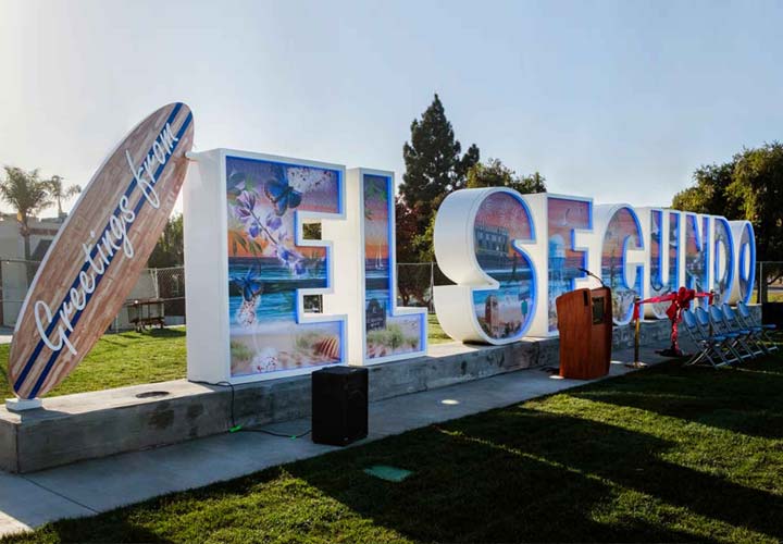 Large El Segundo freestanding sign with beach scenes and a surfboard design.