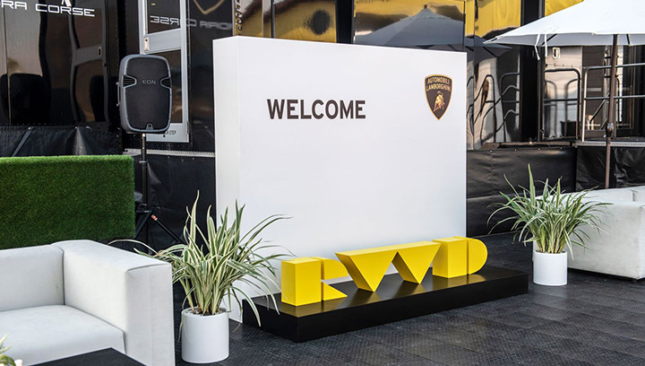 A freestanding sign for an outdoor event with a white welcome wall and a yellow logo.