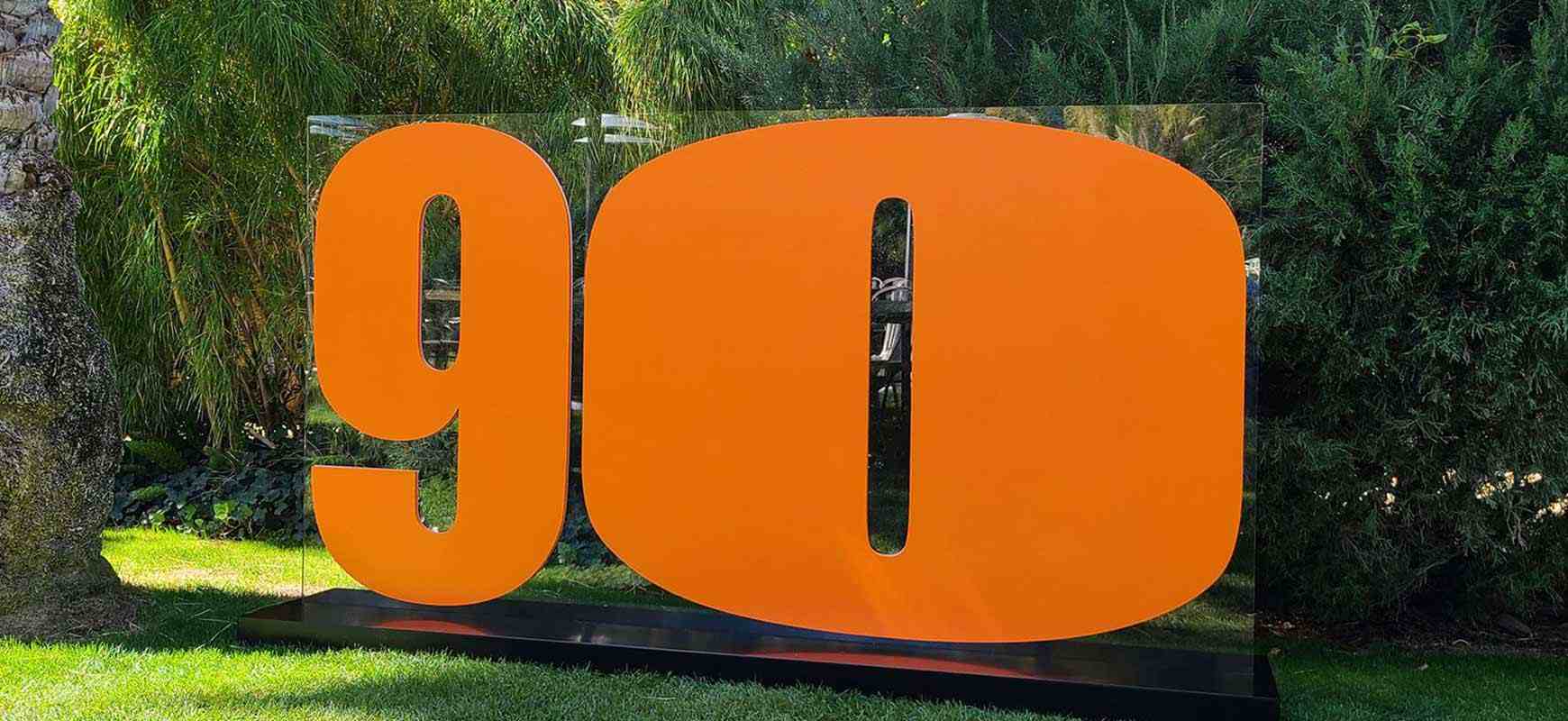 Orange freestanding sign featuring the number ninety, made of acrylic and installed in the yard.