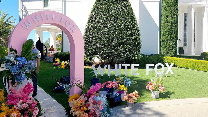 Pink event freestanding sign with a White Fox cutout logo and colorful flowers.