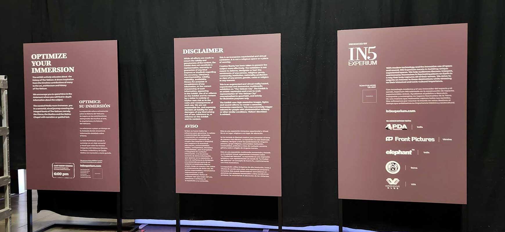 Three tall, dark red freestanding signs with a list of sponsors and a QR code.